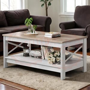 May include: A rectangular coffee table with a light wood-toned top and a white frame featuring X-shaped side supports. The table includes a lower shelf holding a dark lantern, a stack of books, and a bouquet of white flowers in a glass vase.
