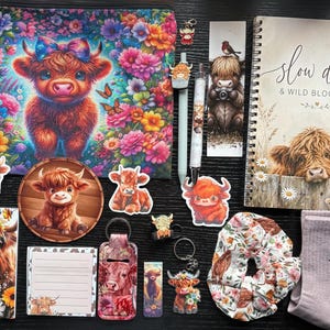 Puede incluir: Un conjunto de papelería y accesorios con imágenes de ganado Highland, que incluye un estuche con cremallera, un cuaderno de espiral con el texto "slow days & WILD BLOOMS", pegatinas, un bolígrafo, un llavero, un coletero y calcetines de color lila.