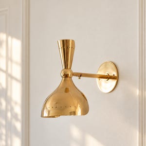 May include: A polished brass wall sconce featuring a dual-cone design with a wide, downward-facing shade and a smaller upward-facing cone, both accented with a row of small perforations along the edges, mounted on a circular wall plate.