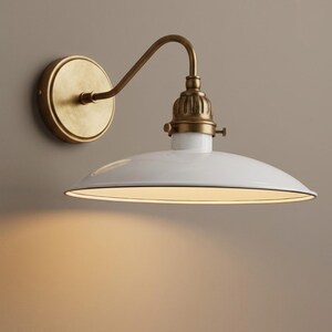 Könnte beinhalten: Eine Wandleuchte mit einem weißen, schalenförmigen Schirm und einem messingfarbenen Arm und einer Montageplatte. Die Leuchte ist im Vintage-Stil gehalten und wirft ein warmes Licht nach unten. Sie ist an einer neutralfarbenen Wand montiert.