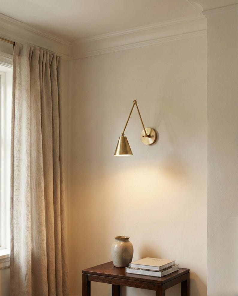 May include: A brass wall-mounted lamp with an adjustable articulated arm and a conical shade. The lamp features a circular wall plate and emits a warm downward light. The fixture is constructed from polished brass with a metallic finish.