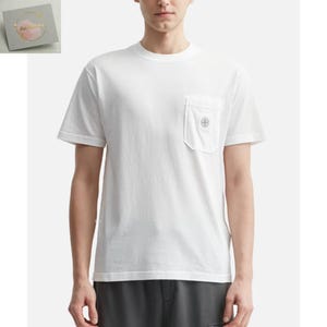 Może przedstawiać: Biały t-shirt z krótkim rękawem z kieszenią na piersi. Kieszeń posiada okrągły emblemat. Koszulka wykonana jest z gładkiej, jednolitej tkaniny. Model ma na sobie szare spodnie.