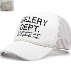 Puede incluir: Gorra de camionero blanca con el texto "GALLERY DEPT." en negro, y la dirección 1613 Beverly Blvd, Los Ángeles, CA 90036. La gorra tiene un panel frontal y una visera blancos, con una parte trasera de malla y un detalle de cuerda.