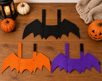 May include: Three sets of felt bat wings in black, orange, and purple. Each set features a central wing piece with jagged edges and two vertical straps with black hook-and-loop fasteners attached to the top for securing the accessory.