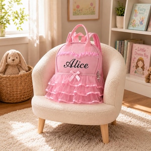Op de afbeelding: Een roze rugzak met een gelaagde tule afwerking, een kleine strik in het midden en de naam Alice geborduurd in zwarte letters. De tas is voorzien van handvatten aan de bovenkant, verstelbare schouderbanden en een ritssluiting met een bedeltje.