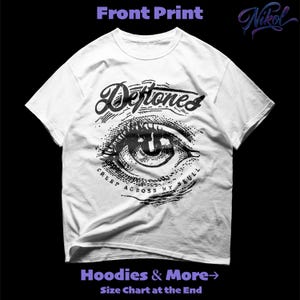 Puede incluir: Camiseta blanca con un diseño de ojo negro y la palabra "Deftones" arriba. Debajo, el texto "Creep Across My Skull". También incluye "Hoodies & More" y "Size Chart at the End".