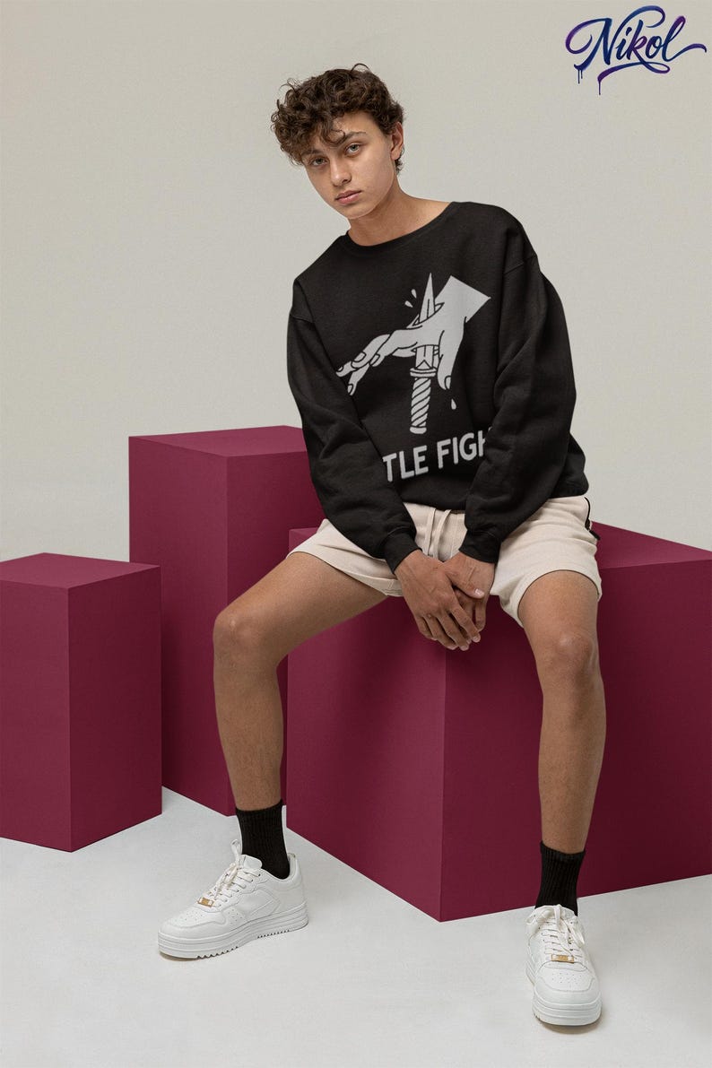Model wearing a white long-sleeve shirt in a relaxed seated pose, displaying title fight on the front.