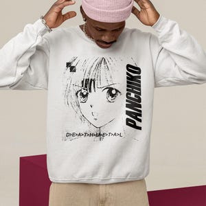 Close-up lifestyle mockup of a white sweatshirt with panchiko deathmetal album front print, model adjusting beanie.