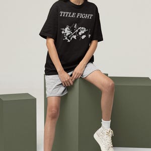 Model leaning in a studio setting wearing a white long-sleeve top with Title Fight on the front.