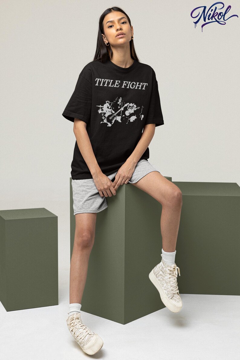 Model leaning in a studio setting wearing a white long-sleeve top with Title Fight on the front.