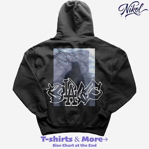 Puede incluir: Una sudadera con capucha negra con un gráfico en la espalda que presenta una silueta dentro de un marco rectangular y texto blanco estilo grafiti que dice "LA". La sudadera también tiene el texto "T-shirts & More" en la parte inferior.