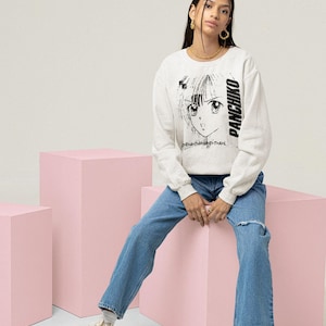Model sitting in a studio setting wearing a white long-sleeve top, front print featuring panchiko deathmetal album.