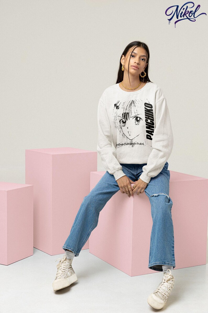 Model sitting in a studio setting wearing a white long-sleeve top, front print featuring panchiko deathmetal album.