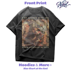 May include: Dark gray t-shirt with a rectangular graphic featuring a classical painting. The text "I NO LONGER FEAR THE" and "RAZOR GUARDING MY HELL" are printed above and below the image. The brand name "Nikol" is in the upper right corner.