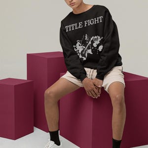 Seated lifestyle shot of a white long-sleeve shirt, highlighting Title Fight on the front print zone.