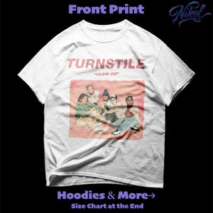 Può includere: T-shirt bianca con il nome della band "TURNSTILE" in rosa sopra una grafica dei membri della band. Il testo "GLOW ON" è sotto. La maglietta ha anche il testo "Hoodies & More" e "Size Chart at the End".