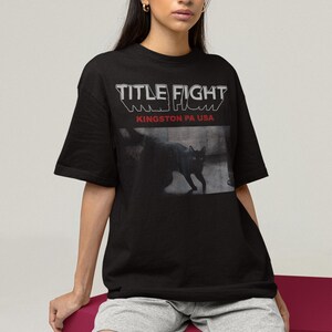 Studio lifestyle shot of a white pullover sweatshirt with Title Fight centered on the front.