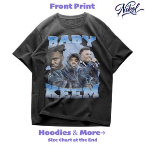 May include: Black t-shirt with a graphic featuring three people and the text "BABY KEEM" in a blue and white design. The shirt also has the text "Hoodies & More" and "Size Chart at the End".