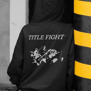Casual outfit photo with a white short-sleeve t-shirt and Title Fight printed on the front, studio background.