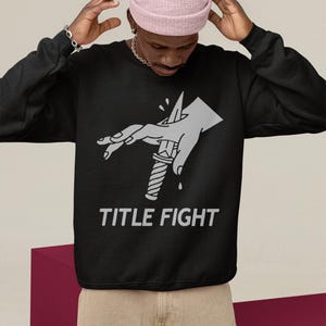 Indoor lifestyle shot of a white hooded sweatshirt from behind, featuring title fight as the back print.