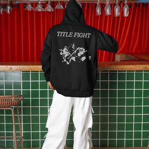 Model wearing a white unisex t-shirt with Title Fight printed on the front, neutral studio background.