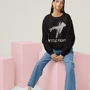 Studio lifestyle shot of a white long-sleeve t-shirt, front print preview featuring title fight.