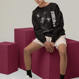 Seated model wearing a white unisex long-sleeve tee with Panchiko deathmetal album front print in a studio setting.
