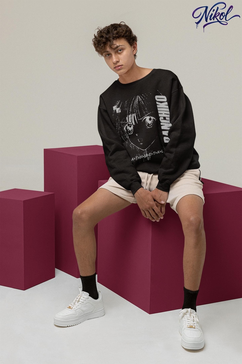 Seated model wearing a white unisex long-sleeve tee with Panchiko deathmetal album front print in a studio setting.