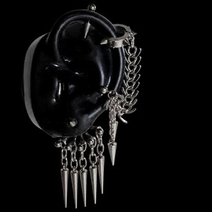 Puede incluir: Un conjunto de pendientes y ear cuff plateados con múltiples puntas metálicas colgantes y eslabones de cadena. La joyería incluye un aro con púas en la parte superior y una serie de cinco puntas verticales que cuelgan de la parte inferior.