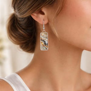 Peut inclure: Boucles d'oreilles rectangulaires argentées avec un motif marbré dans les tons or, marron et gris. Les boucles d'oreilles sont suspendues à un crochet argenté. Le motif marbré donne aux boucles d'oreilles un aspect unique et artistique.