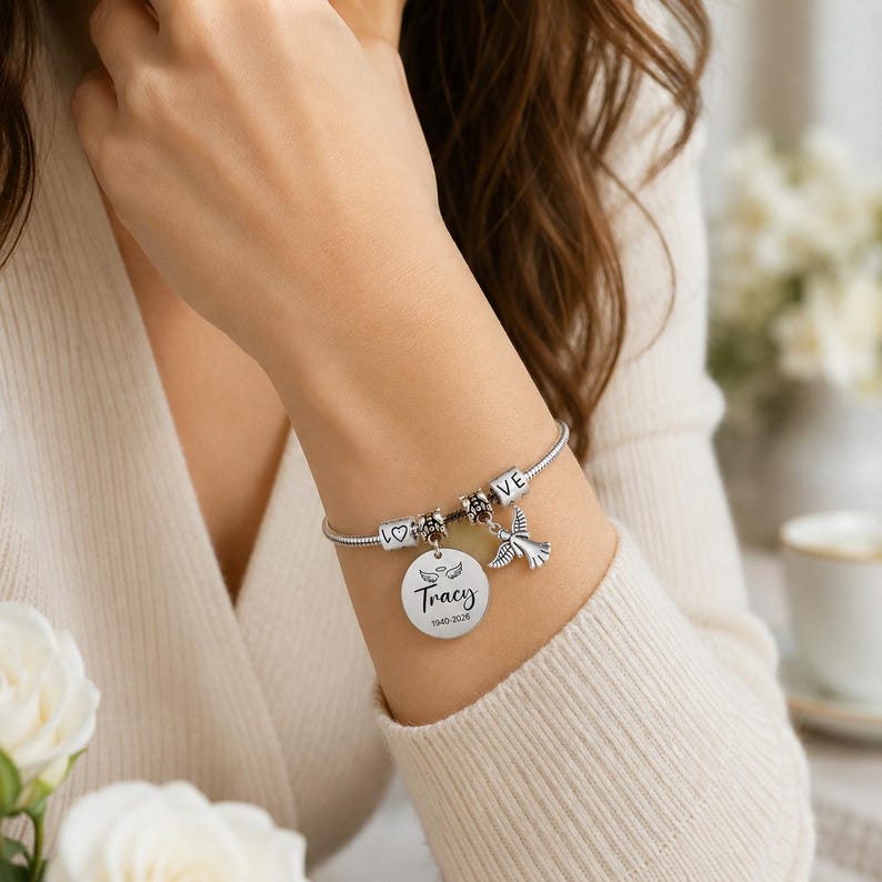 Peut inclure: Un bracelet &agrave; breloques en cha&icirc;ne serpent argent&eacute;e avec un pendentif rond grav&eacute; du nom Tracy, des ann&eacute;es 1940-2026 et de petites ailes d'ange. Le bracelet comprend des perles carr&eacute;es suppl&eacute;mentaires avec le texte LOVE et un symbole de c&oelig;ur.