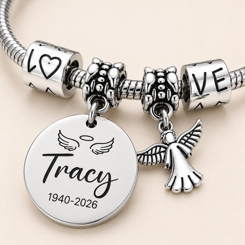 Peut inclure: Un bracelet &agrave; breloques argent&eacute; avec un pendentif rond grav&eacute; du nom Tracy, des ann&eacute;es 1940-2026, et une paire d'ailes d'ange avec une aur&eacute;ole. Le bracelet comprend une petite breloque ange et deux perles cylindriques portant l'inscription LOVE.