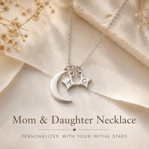 Puede incluir: Un collar de tono plateado que presenta un dije de media luna y dos dijes de estrella de cuatro puntas. Cada dije de estrella está grabado con una letra individual, A y C. El collar incluye una cadena delicada y el texto Mom & Daughter Necklace.