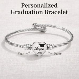 May include: A silver-coloured, personalised graduation bracelet. The bracelet has a heart-shaped charm with the name "Megan" and the year "2026" engraved. The text "Personalized Graduation Bracelet" is at the top.