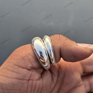 May include: A shiny, silver ring with a double-band design. The ring has a smooth, polished surface, reflecting the surrounding environment. The ring is a piece of jewelry.