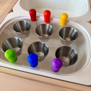 May include: A set of three ceramic mugs with a speckled, matte finish. The mugs are in shades of cream, light gray, and dark gray. Each mug has a simple, minimalist design and a rounded handle. The mugs are stacked on top of each other.