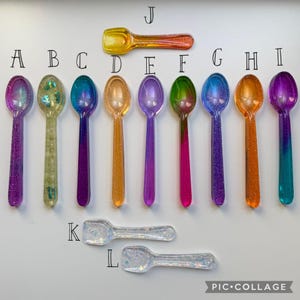 May include: A collection of colorful, glittery resin spoons in various shades, including purple, green, orange, and blue. The spoons are arranged in a row, with a rectangular spoon at the top and two smaller spoons at the bottom. The spoons are likely for decorative purposes.