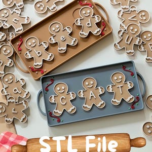 May include: A set of tan gingerbread-shaped letter tiles featuring white icing details and letters, arranged on two rectangular trays in tan and blue. The trays feature red and green decorative swirls. The text STL File is visible.