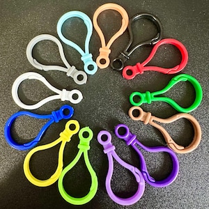 May include: A collection of twelve plastic lobster claw clasps arranged in a circular pattern. The clasps are available in various solid colors including black, white, gray, red, orange, yellow, light blue, green, lime green, purple, blue, and tan.