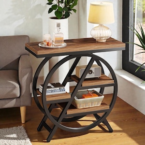 May include: A brown and black side table with a circular design. The table has a rectangular top with a lamp, a decanter, and glasses. The table has three shelves with a radio, books, and a basket. The table is 30 inches long, 12 inches wide, and 30 inches high.