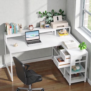 May include: A white L-shaped desk with a black office chair. The desk has a laptop, books, and a printer. There are drawers and shelves for storage. A small plant and a window are visible in the background.