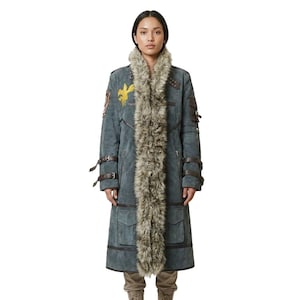May include: A long, gray suede coat with a faux fur collar. The coat features brown leather straps, pockets, and a yellow emblem on the left shoulder. The coat is knee-length and has a tailored fit.