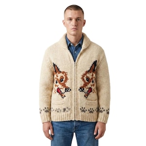 Puede incluir: Un cárdigan de punto grueso color crema con cremallera, cuello de chal y dos bolsillos delanteros. El suéter presenta un patrón de intarsia repetido de caras de zorro en marrón, negro y rojo, con una fila de huellas grises en el dobladillo.