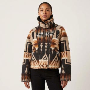 May include: A cropped jacket featuring a geometric pattern in shades of brown, black, and cream. The jacket has a high collar with a buckle strap, long sleeves, and a diagonal front zipper closure, constructed from a thick, textured fabric.