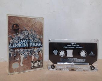 May include: A cassette tape and its case are displayed. The case has a brown and white design with the text "JAY-Z LINKIN PARK COLLISION COURSE" and a parental advisory warning. The cassette tape is black with white text and the same album title.