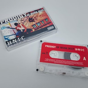 Puede incluir: Una cinta de cassette transparente y su estuche con el álbum "H.N.I.C" de Prodigy of Mobb Deep. La cinta tiene una etiqueta roja con texto blanco. El estuche muestra la carátula del álbum con una persona y el título.