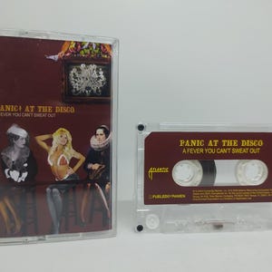 May include: A clear cassette tape case and cassette featuring the album "A Fever You Can't Sweat Out" by Panic! at the Disco. The cover art shows three figures and the album title. The cassette tape is also visible.