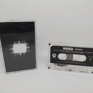 May include: A clear cassette tape with a black label featuring the band name "TOOL" and album title "ÆNIMA". The cassette case is open, with the cover showing a black background and a white square design.