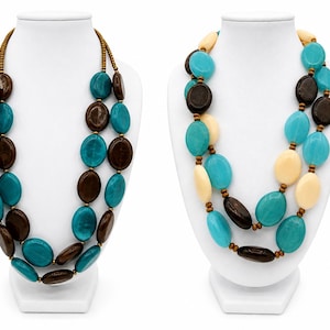 May include: Two multi-strand necklaces displayed on white busts. The left necklace features alternating dark brown and turquoise oval beads. The right necklace features a mix of turquoise, dark brown, and cream-colored oval beads with small brown spacers.
