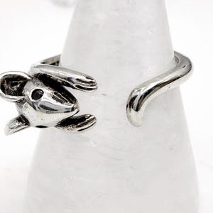 May include: A silver-toned ring featuring a detailed mouse design. The mouse has a small black eye and is wrapped around the finger. The ring is open at the back, allowing for adjustable sizing. The ring is displayed on a white background.